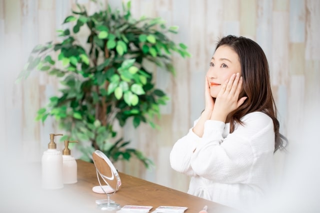 鏡を見ながら化粧品を顔につける女性